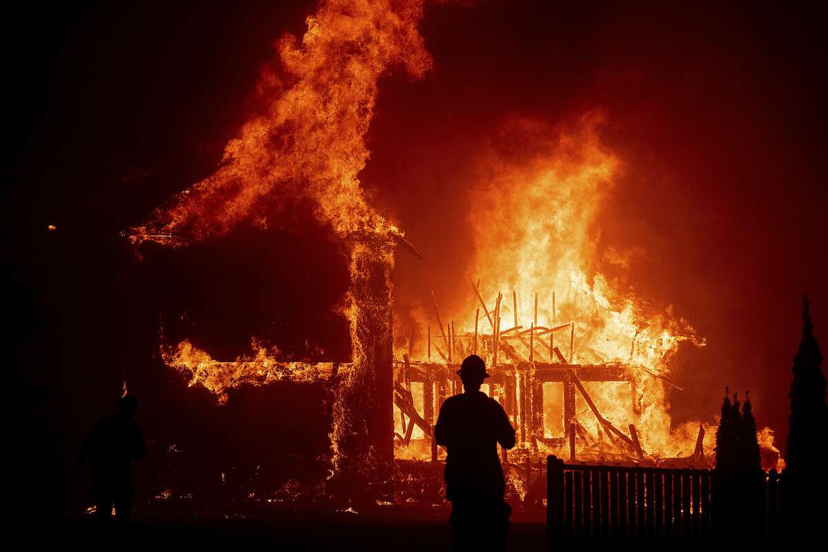 FILE - In this Nov. 8, 2018, file photo, a home burns as the Camp Fire rages through Paradise, Calif. Officials are looking for more stable housing for roughly 600 people still sleeping at a Northern California fairground following the deadly wildfire last year. (AP Photo/Noah Berger, File)