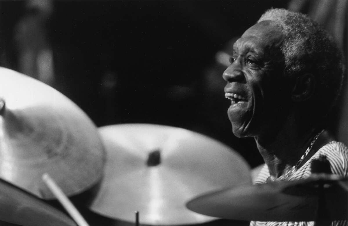Profile headshot of American jazz musician Art Blakey (1919 - 1990) smiling while playing drums during a performance at the Stamford Center for the Arts, Stamford, Connecticut. Cymbals are visible in the foreground.