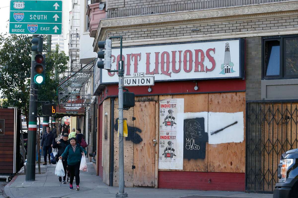 Pedestrians walk along Columbus Avenue past a boarded up storefront with Coit Liquors signage above it on Tuesday, January 22, 2019 in San Francisco, Calif.