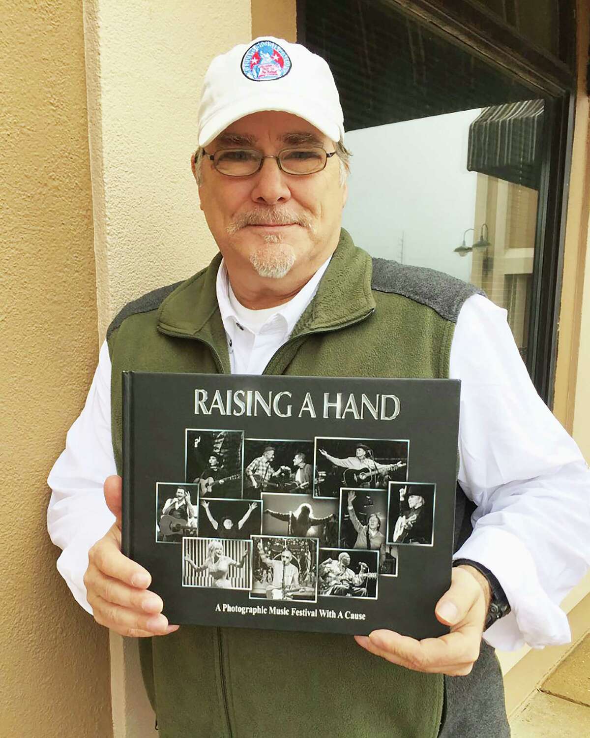 Musician and photographer Kevin Black is holding the book "Raising a Hand for Rett." Black lost his 16-year-old daughter Cortney to Rett Syndrome in 2003. Since then, Black and local photographer Dave Clements have launched the project "Raising a Hand for Rett" where they photograph music artists raising a hand. Vol. 1 was published in 2016. A second volume was released in July.