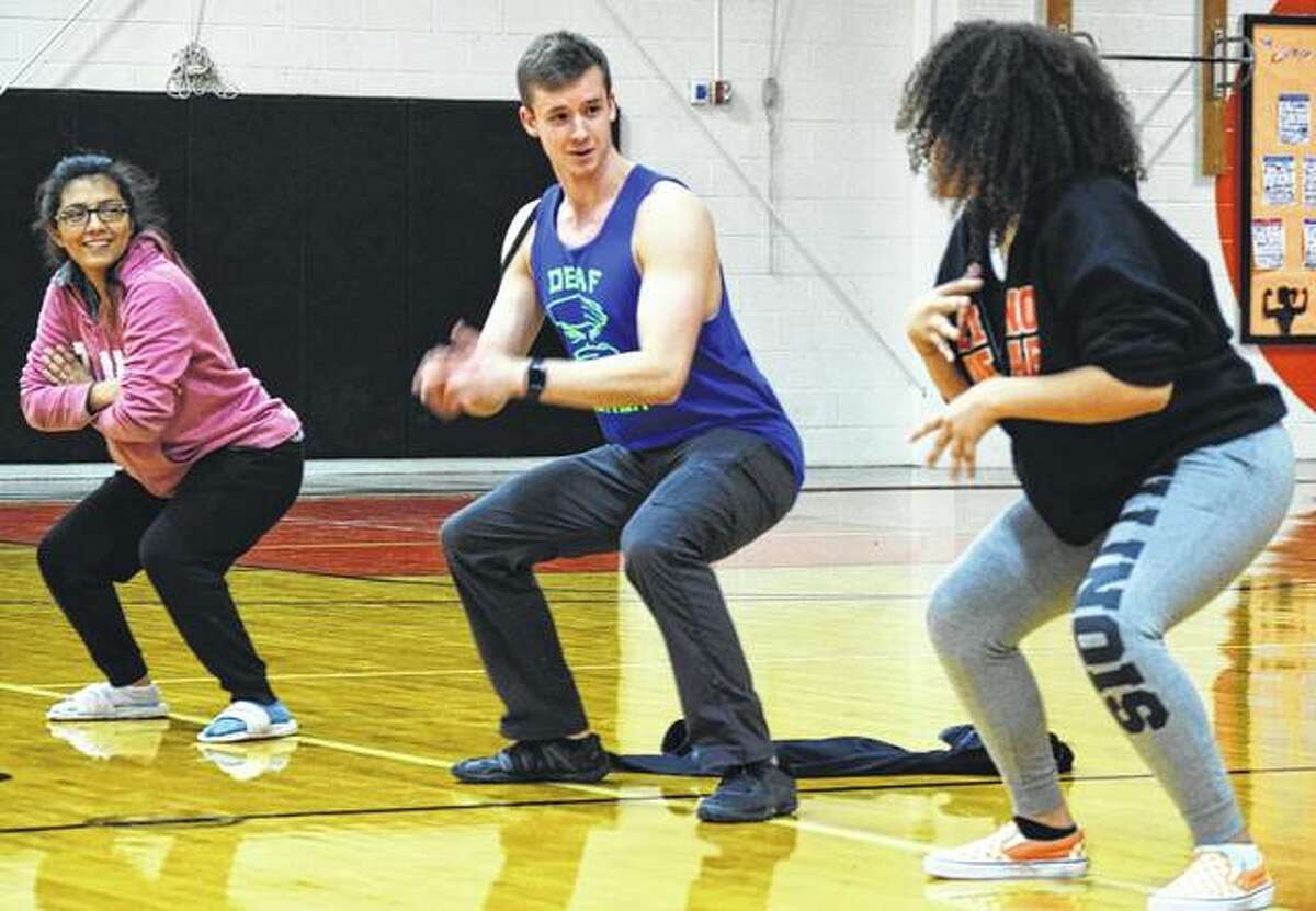 American Ninja Warrior competitor Kyle Schulze has a casual conversation with Estrella Gomez, 17, of Aurora and Kayla Ciganek-Harris, 17, of Chicago, while the three stay in a squat position for as long as they can as part of a challenge on Friday.