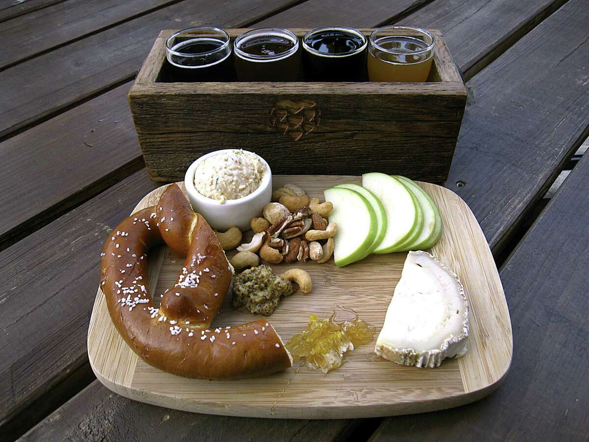 A snack board with a pretzel, obatzde German brie cheese dip, nuts, fruit, honeycomb and goat cheese and a flight of beers from Künstler Brewing.