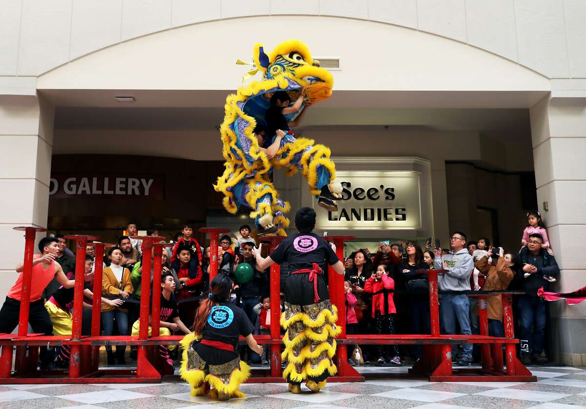 Norman Lau (far left), director of LionDanceME, watches as Jacky Li (center left), 16, and Brandon Wong (center right), 17, leap during their performance at Macy's Center Court at Hillsdale Mall in San Mateo, Calif., on Saturday, January 26, 2019.