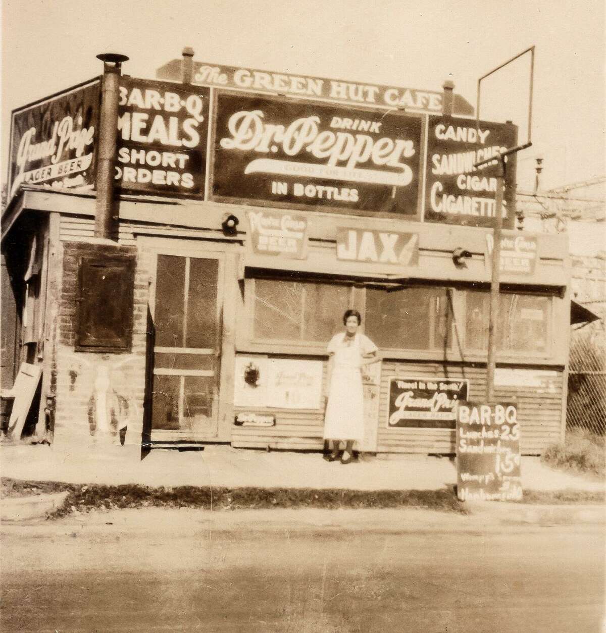 Leona Ginn stands near a vertical brick smoker on the front of The Green Hut Café on Quitman Street in 1934.