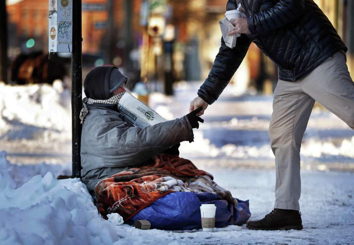 A homeless man outside a coffee shop accepts cash from a customer on a bitter cold morning in Portland, Maine. Instead of helping those crossing the border find asylum, a reader suggests aiding downtrodden Americans.