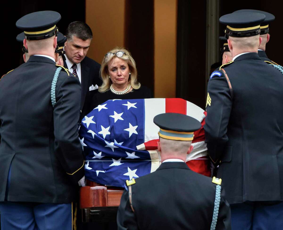 Debbie Dingell waits at the door of Holy Trinity in Washington as her husband's casket is borne into the church.