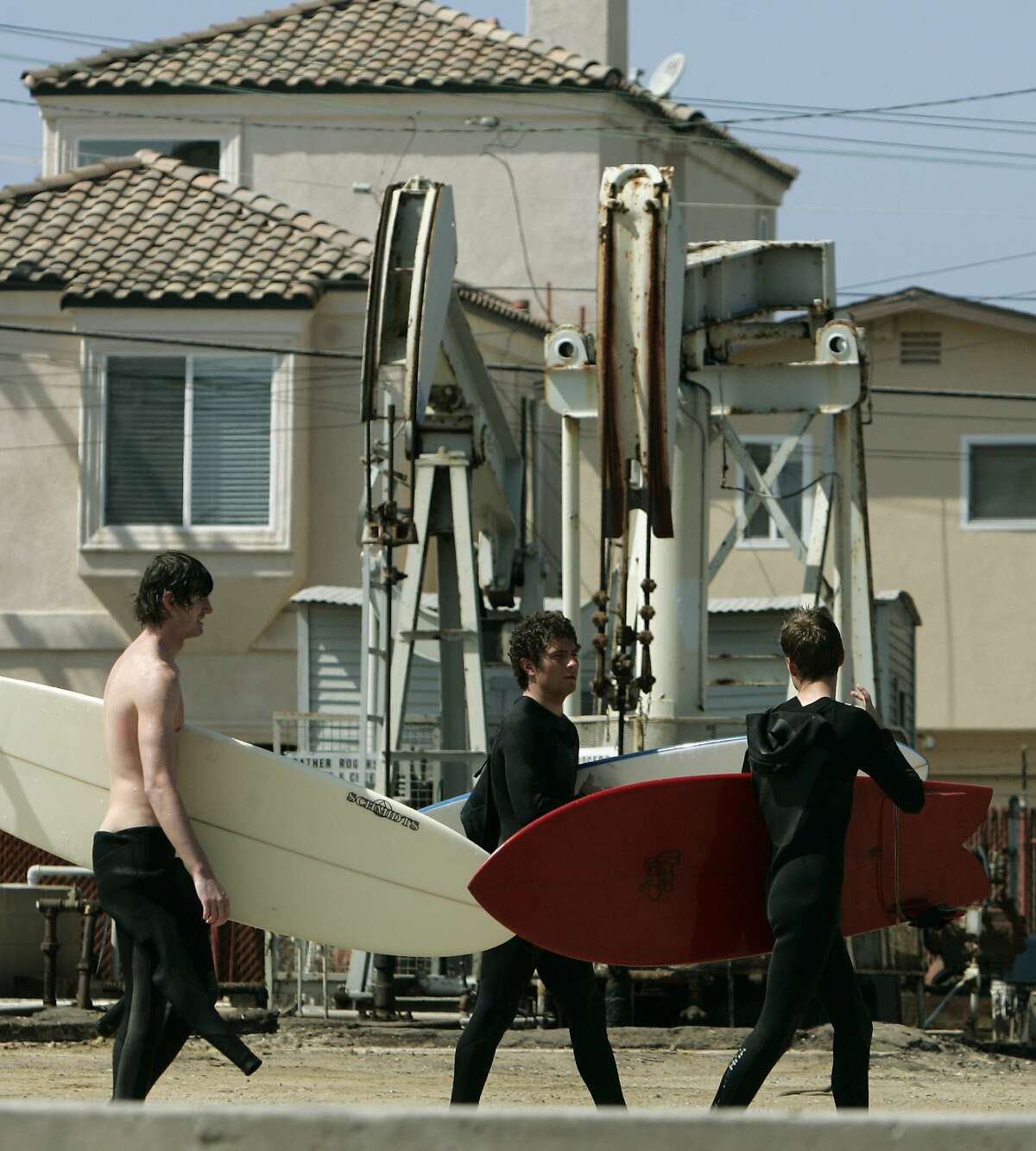 Surfers walk past oil pumps operating next to homes in an area where dozens of oil wells stand side-by-side with homes in the seaside city of Huntington Beach, Calif., also officially known as "Surf City USA," Friday, March 14, 2008. With oil prices at $110 a barrel, producers nationwide are suddenly taking a second look at decades-old wells that were considered tapped out and unprofitable when oil sold for one-fifth the price or less. (AP Photo/Reed Saxon)