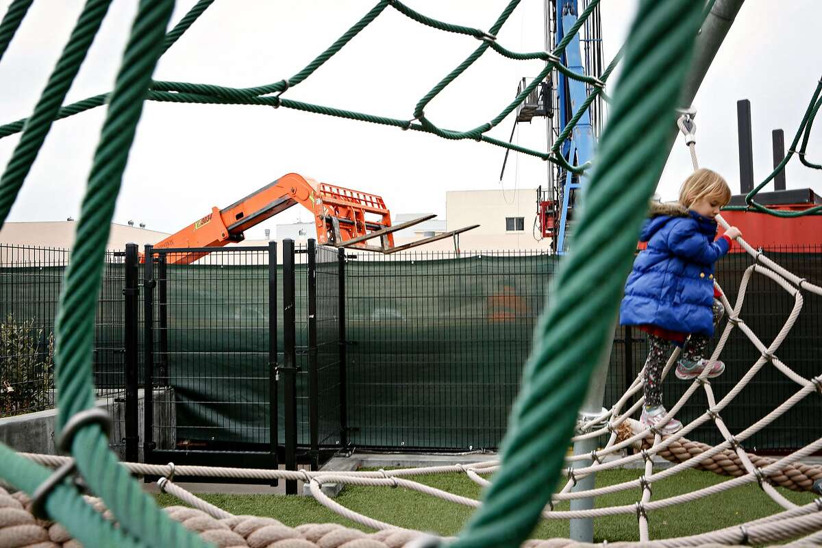 A forklift from a new affordable housing construction site is seen as Josephine Milbrath, 4, plays on the playground at Chan Kaajal Park on Tuesday, February 12, 2019 in San Francisco, Calif. The affordable housing site will be integrated with Chan Kaajal Park.