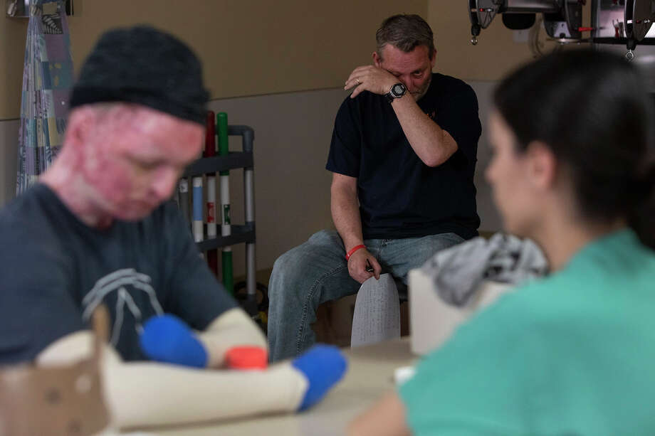 Karl Sutterfield wipes his eyes after reading a letter his son, Zachary Sutterfield, left, wrote to him moments earlier during Zachary's daily physical therapy session. Most of Zachary's fingers had to be amputated due to burns from the fire. He uses a special device to hold a pen. At right is Sarah Flores, a physical therapist at the U.S. Army Institute of Surgical Research Burn Center. Photo: Lisa Krantz / San Antonio Express-News
