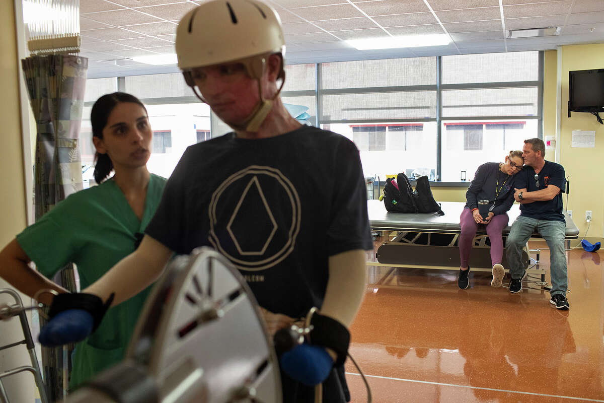 DJ Sutterfield and Karl Sutterfield wait as their son, Zachary Sutterfield, exercises with physical therapist Sarah Flores, left, during his daily rehabilitation session at the U.S. Army Institute of Surgical Research Burn Center.
