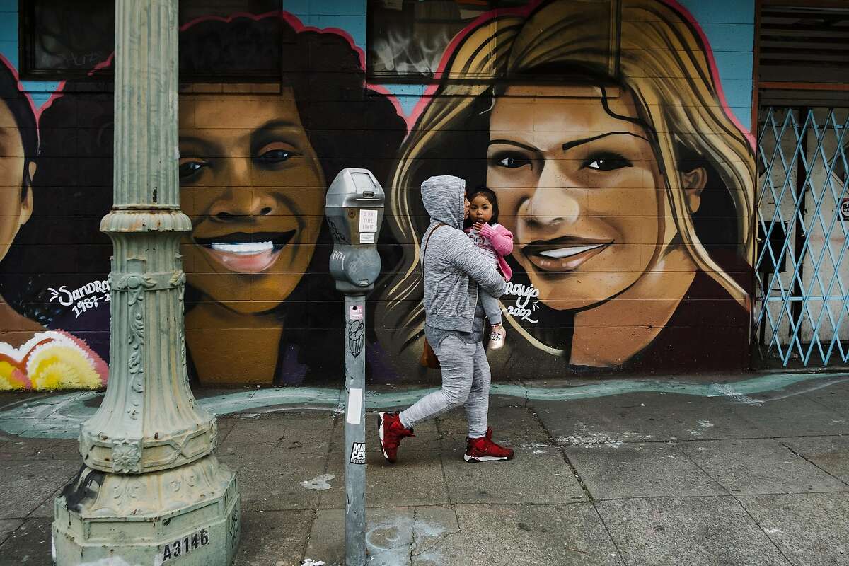 A woman and child walks past a mural on International Boulevard near 23rd Avenue where construction of the new Bus Rapid Transit(BRT) line is ongoing, in Oakland, Calif., on Tuesday, February 12, 2019.