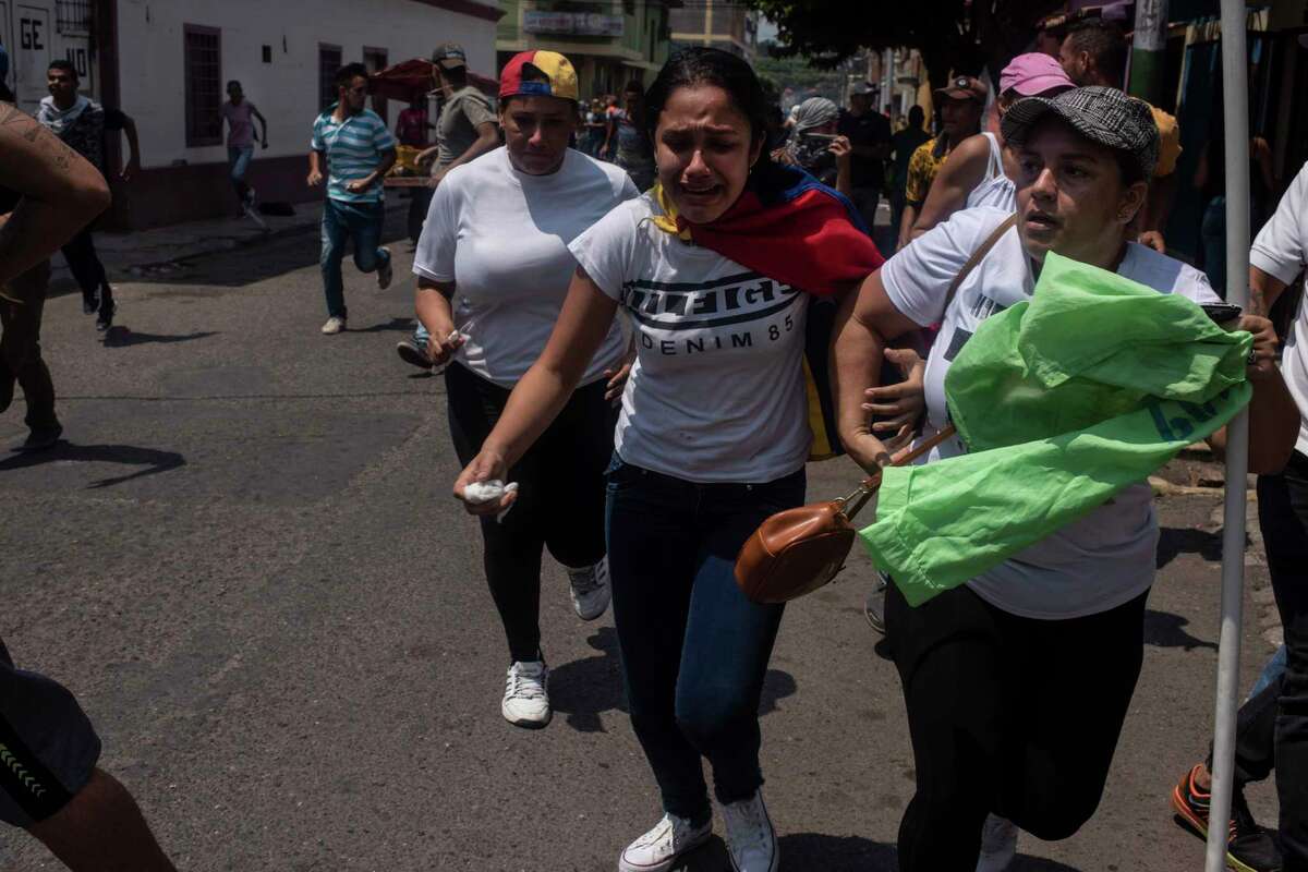 Women run from armed pro-government militias on motorcycles in San Antonio, Venezuela, on Saturday.