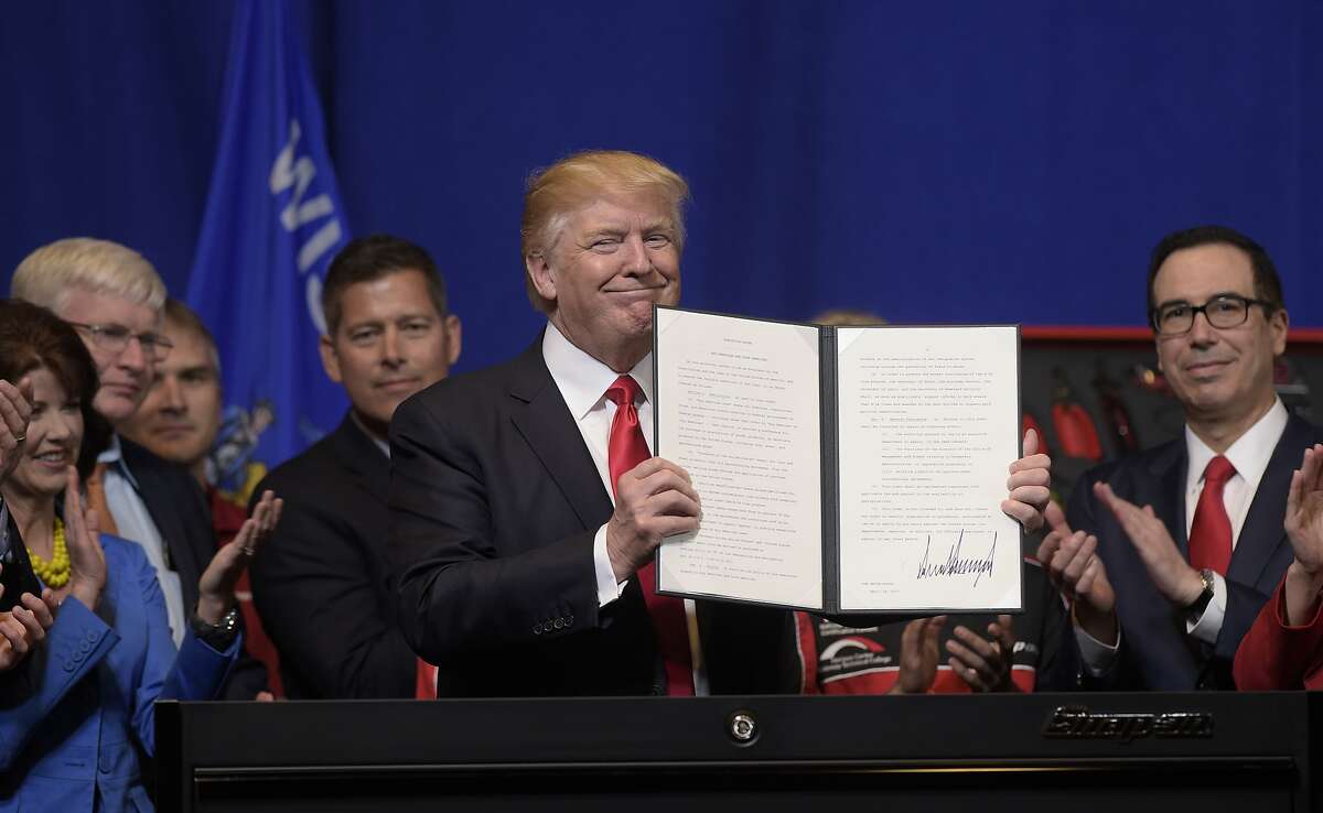 FILE - In this April 18, 2017 file photo, President Donald Trump holds up the "Buy American, Hire American" executive order which he signed during a visit to the headquarters of tool manufacturer Snap-on Inc. in Kenosha, Wis. Immigrants with specialized skills are being denied work visas or seeing applications get caught up in lengthy bureaucratic tangles under federal changes that some consider a contradiction to Trump’s promise of a continued pathway to the U.S. for the best and brightest. (AP Photo/Susan Walsh)