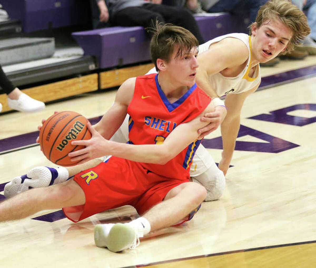 Roxana’s Andrew Beckman (left) looks for a teammate after going to the floor to reclaim a loose ball ahead of CM’s Bryce Zupan in the second half of the Breese Central Class 3A Regional quarterfinal game Monday night in Breese.