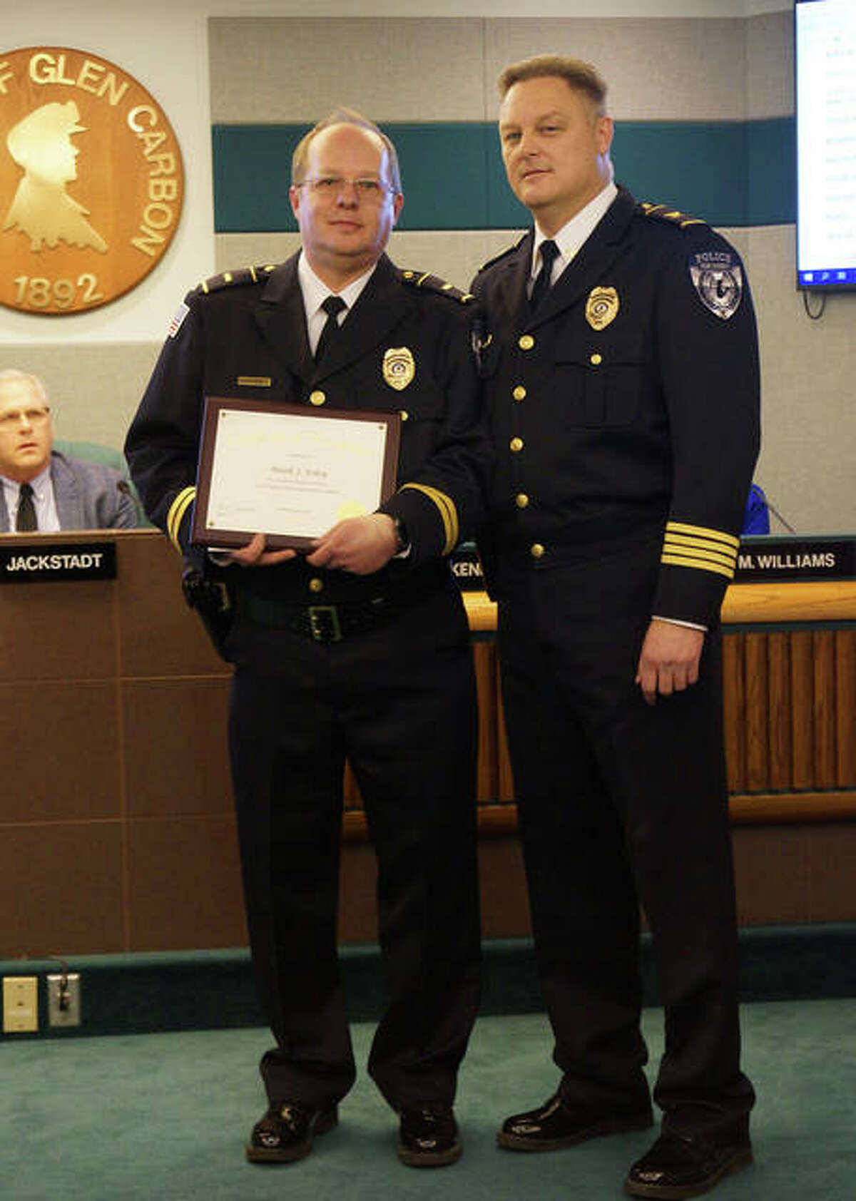 Glen Carbon Police Lt. Mark Foley received a plaque Tuesday, honoring him for 30 years of service to the department. With him is Police Chief Todd Link, right. In the background is Mayor Rob Jackstadt.