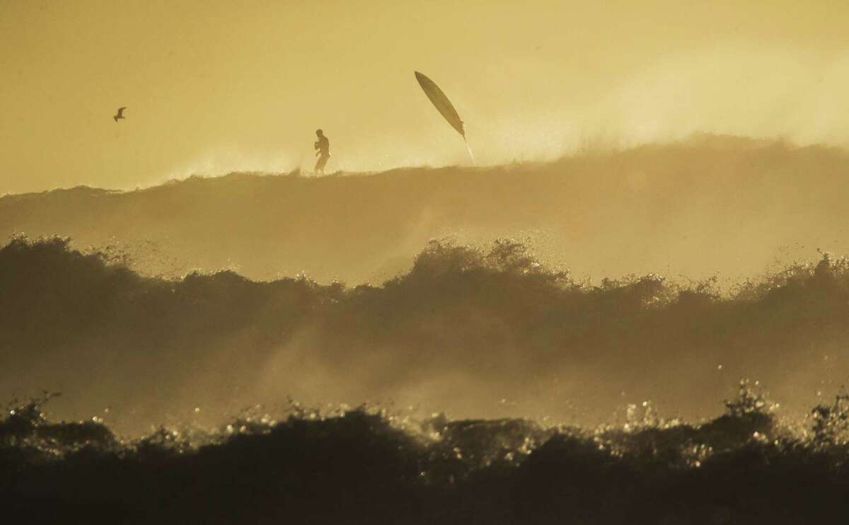A man stands on a paddleboard while a surfer loses his surfboard at Mavericks Beach, where waves were 20-30 feet high on Wednesday, Dec. 19, 2018, in Half Moon Bay, Calif.