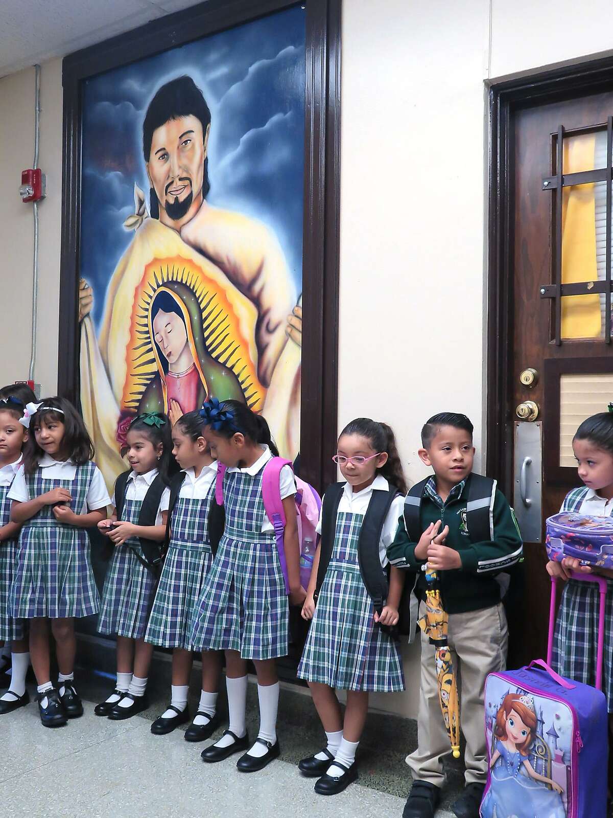 Students at Our Lady of Guadalupe Catholic School stand by a mural of Juan Diego and Our Lady of Guadalupe as they wait to be escorted to their classroom on the first day of the school year.