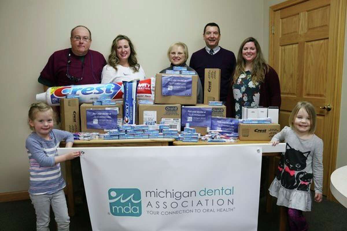 Dr. Chris Jones (rear left) poses among others with thousands of toothbrushes and tubes of toothpaste to be handed out to area kids. (From left) Mila Konkus, 4; Chris Jones, doctor of dental surgery; Camille Secor, doctor of medicine in dentistry; Cynthia Young of Midland Public Schools; Larry Eischer from Crest/OralB; Jane Harrington from Jones & Secor Family Dentistry and Cate Tierney, 4. (photo provided)