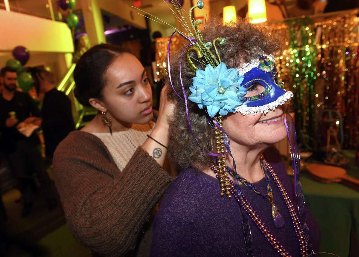 Liah Sinquefield, left, of Lotta Studio assists Renate O’Hair of Wolcott with her mask during the Mardi Gras celebration at the Mitchell Library branch in New Haven Tuesday.
