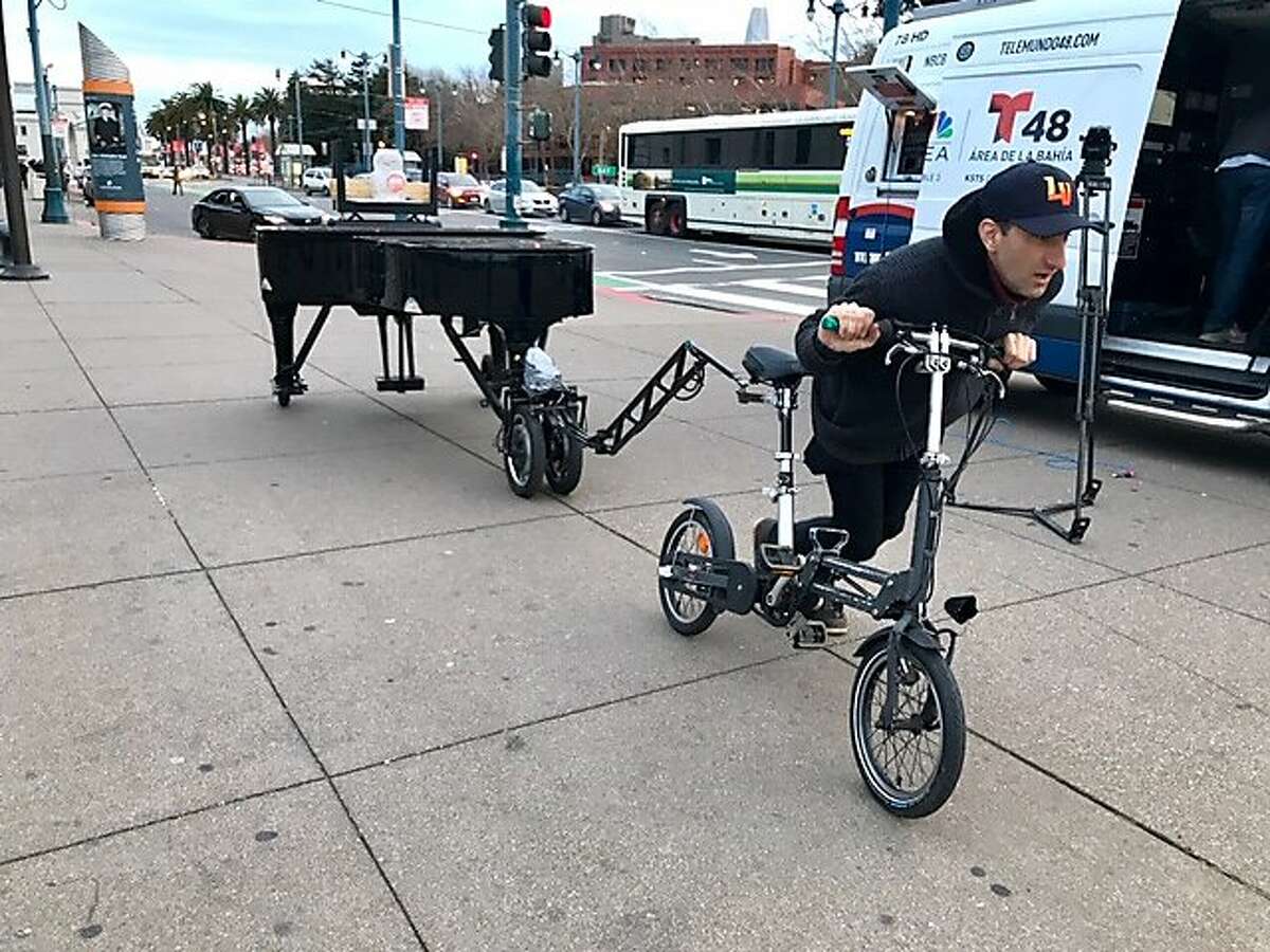 Davide Martello pushes his bicycle, which is towing a grand piano, along the Embarcadero in San Francisco on March 7, 2019.