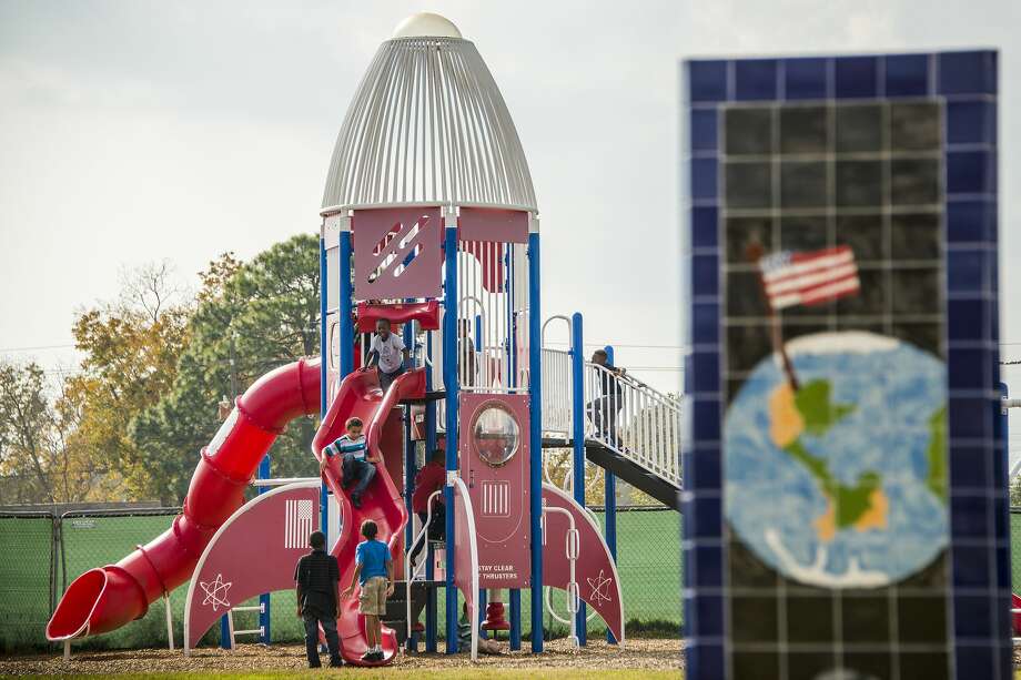 Behind one of seven obelisks displaying student art work depicting a space theme, students at McWhirter Elementary play on rocket-shaped playground equipment on Monday, Dec. 15, 2014, in Webster. Photo: File