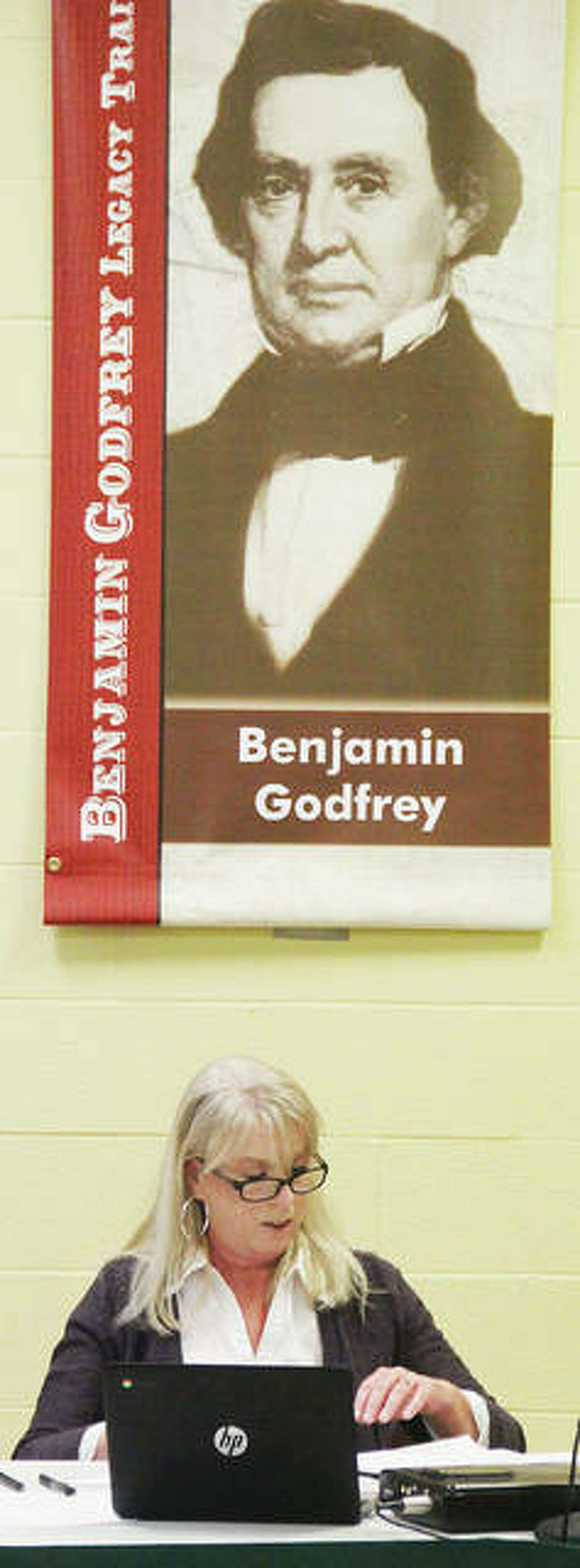 New Godfrey Village Clerk Bethany Bohn sits under a banner for town namesake Benjamin Godfrey after been sworn in at Tuesday’s Village Board meeting. She replaces long-time clerk Pam Whisler, who retired in December and had been the only person to hold the position until Tuesday.
