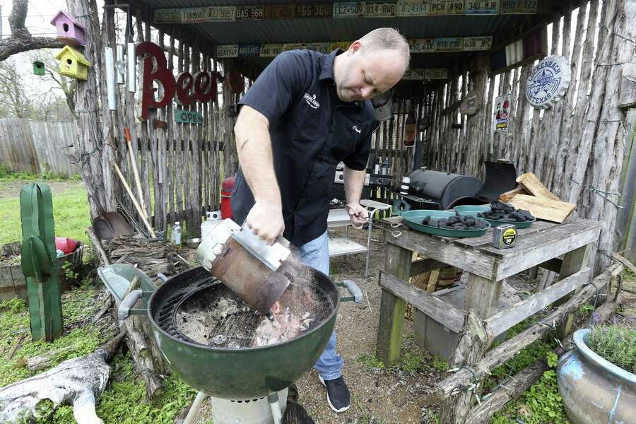 Chuck Blount pours charcoal briquettes from a chimney starter into a Weber grill as he prepares to grill chicken and sausage with an off-set fire, with all the briquettes placed on one side of the grill.