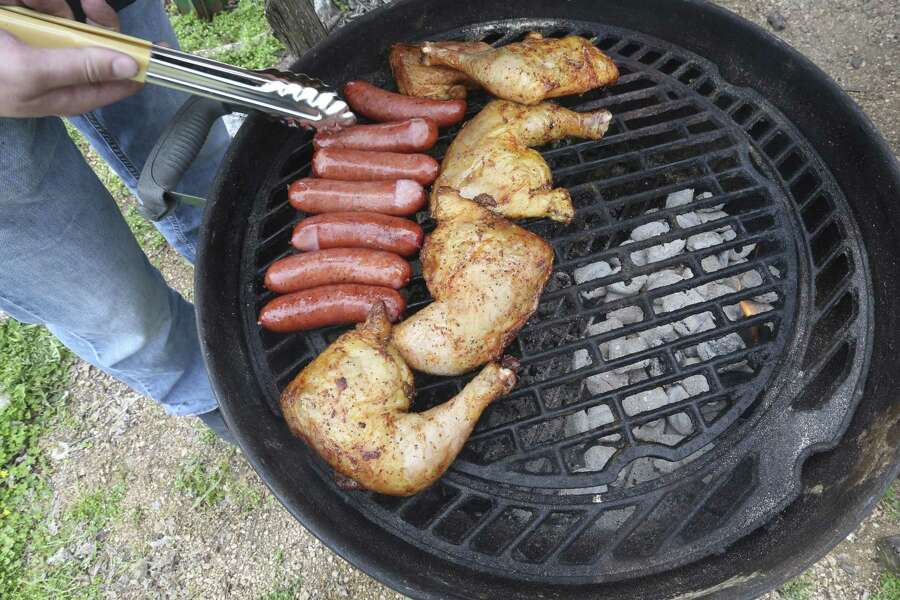 Sausage and chicken cook over indirect heat in a Weber grill.