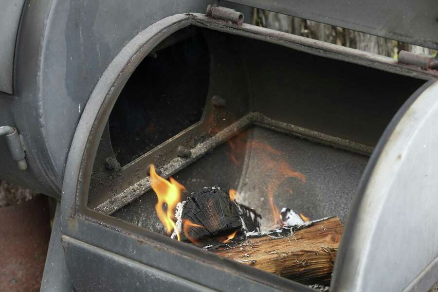 Two split logs rest on a small pile of charcoal briquettes to get an offset smoker to the correct 250 degree temperature.