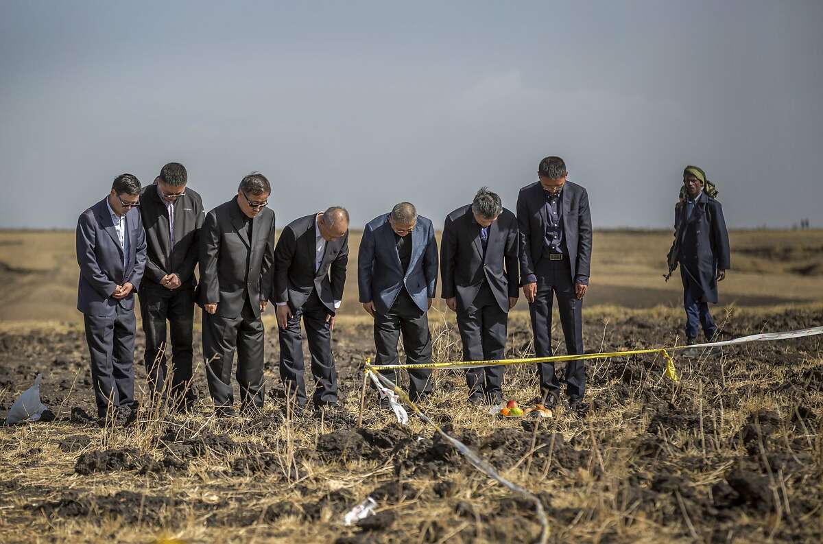 Officials from the Aviation Industry Corporation of China (AVIC) pray next to an offering of fruit, bread rolls, and a plastic container of Ethiopian Injera, a fermented sourdough flatbread, placed next to incense sticks, at the scene where the Ethiopian Airlines Boeing 737 Max 8 crashed shortly after takeoff on Sunday killing all 157 on board, near Bishoftu, or Debre Zeit, south of Addis Ababa, in Ethiopia Tuesday, March 12, 2019. Ethiopian Airlines had issued no new updates on the crash as of late afternoon Tuesday as families around the world waited for answers, while a global team of investigators began picking through the rural crash site. (AP Photo/Mulugeta Ayene)
