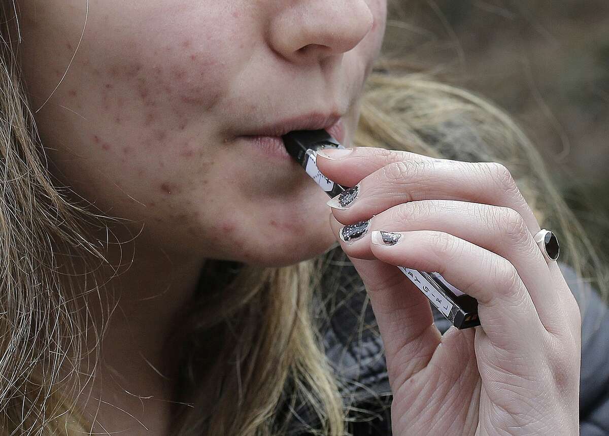 FILE - In this April 11, 2018, file photo, a high school student uses a vaping device near a school campus in Cambridge, Mass. U.S. health regulators are moving ahead with a plan to keep e-cigarettes out of the hands of teenagers by restricting sales of most flavored products in convenience stores and online. (AP Photo/Steven Senne, File)