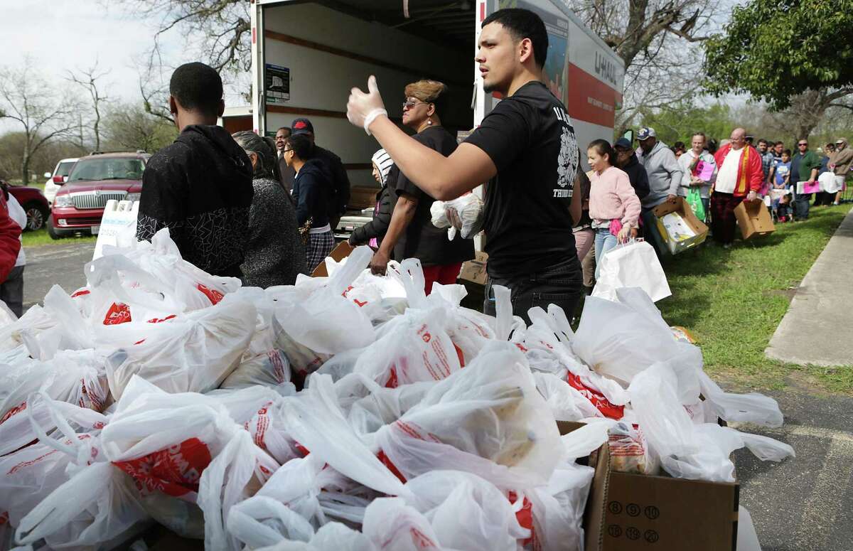 Jonathan Torres, center, of Wagner H.S., hands out bags of vegetables to people waiting in line, as Blessed Angels, also known as "Emergency Food Pantry", hosts a food giveaway, also sponsored by Omega Psi Phi fraternity, Judson Independent School District and Cheesecake Factory, for seniors, veterans and the homeless, on Monday, March 12, 2018, at Alamo United Methodist Church. Some 750 families in need were allowed to come pickup food. Around 150 volunteers were present to help run the event.