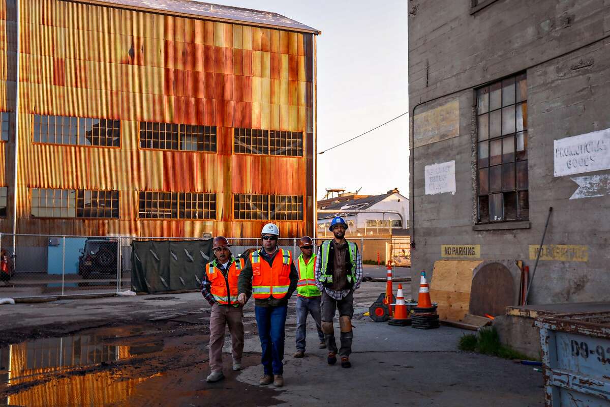 Workers walk past historic industrial buildings at Pier 70 in San Francisco, California, on Wednesday, March 13, 2019. Many buildings have been restored or will be restored in the area.