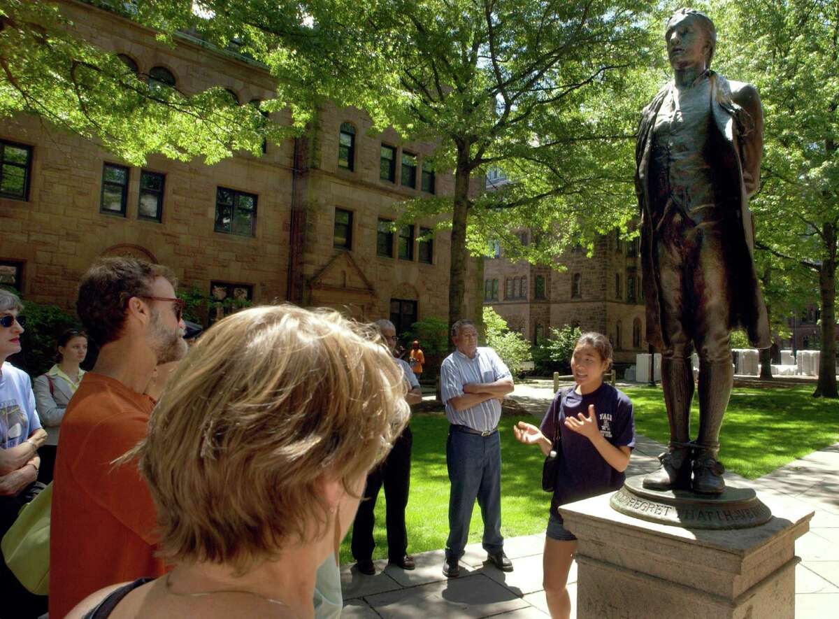 Visitors standing by a statue of Yale graduate Nathan Hale, conducts a walking tour of Yale and the Old Campus to visitors.