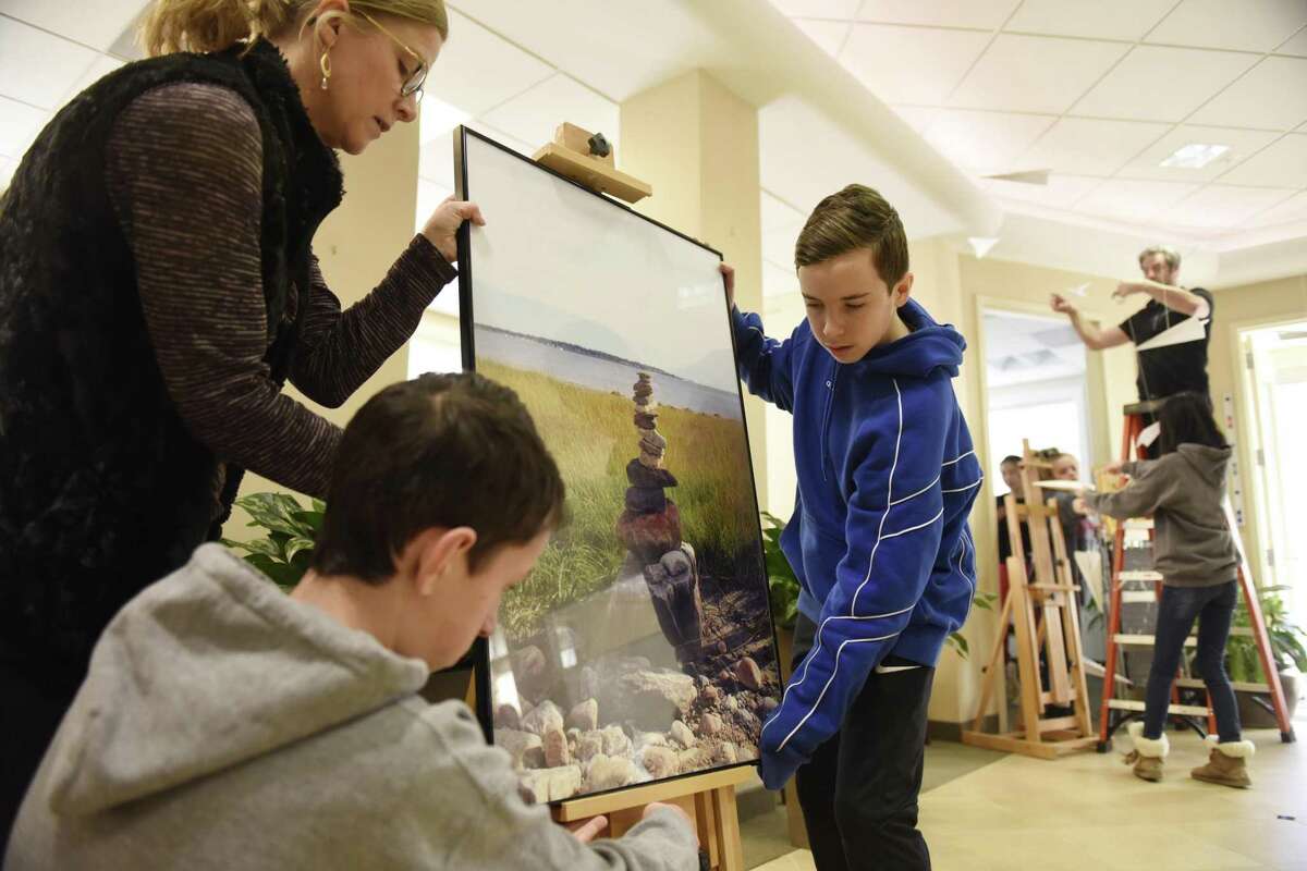 Eastern Middle School art teacher Stacey Cleary and eighth-graders Luke McQuillan, center, and Nicholas O’Brien set up a photograph from Tod’s Point for their art show “A Line in the Sand” at First Bank of Greenwich in Cos Cob.