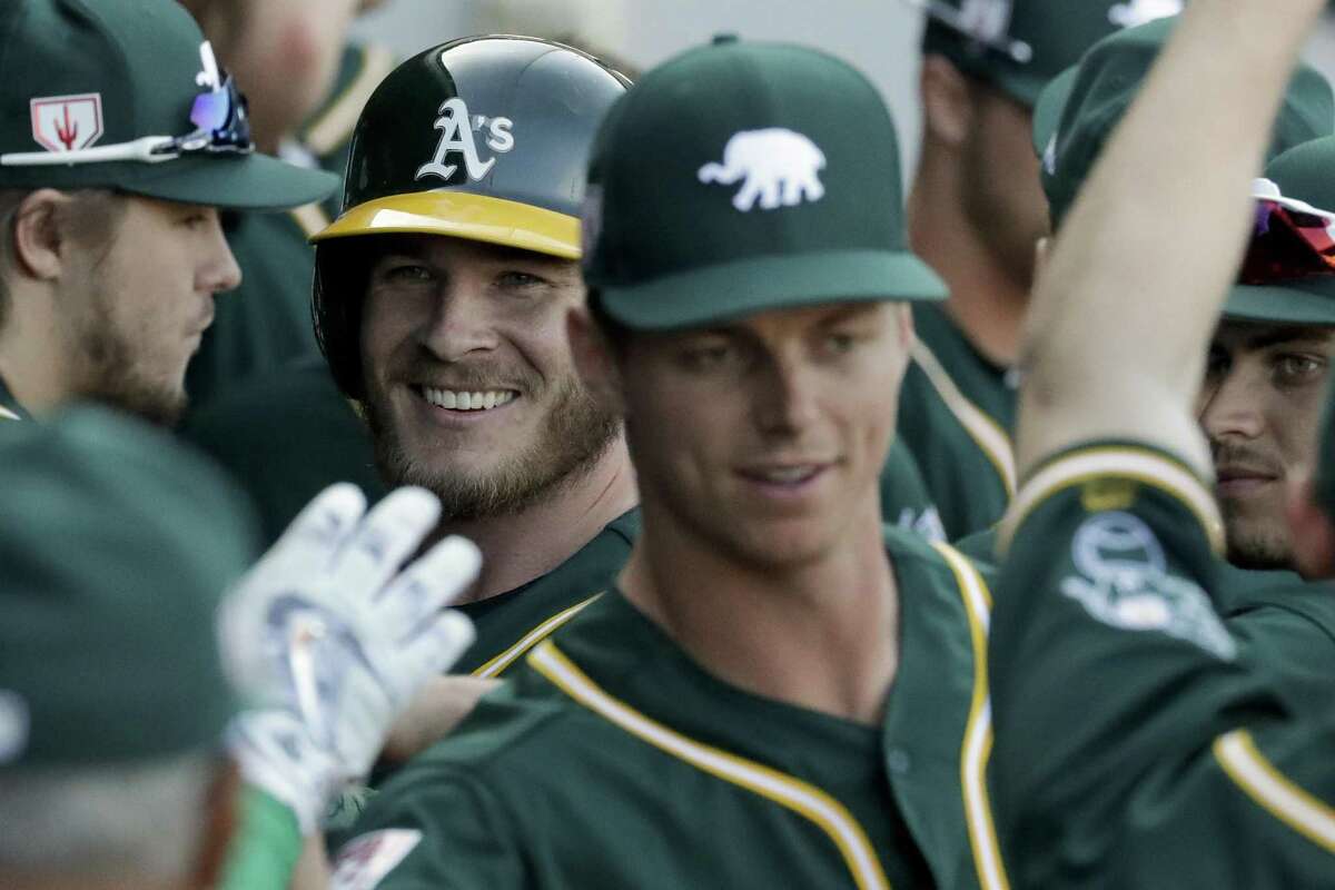 Oakland Athletics' Chris Herrmann, left, celebrates in the dugout after scoring on a ball hit by Cliff Pennington during the fifth inning of a spring baseball game in Mesa, Ariz., Thursday, Feb. 28, 2019.
