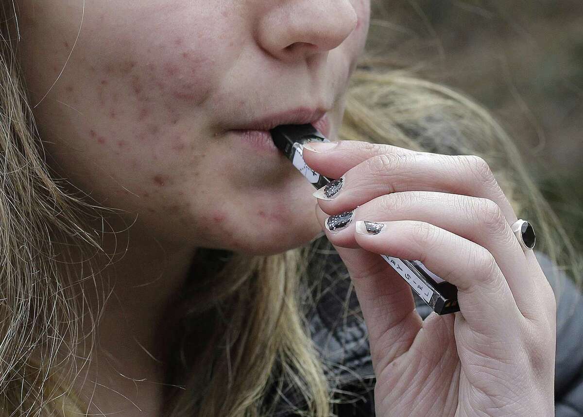 FILE - In this April 11, 2018 file photo, a high school student uses a vaping device near a school campus in Cambridge, Mass. Twice as many high school students used nicotine-tinged electronic cigarettes in 2018 compared with the previous year, an unprecedented jump in a large annual survey of teen smoking, drinking and drug use. Findings were released on Monday, Dec. 17, 2018. (AP Photo/Steven Senne, File)