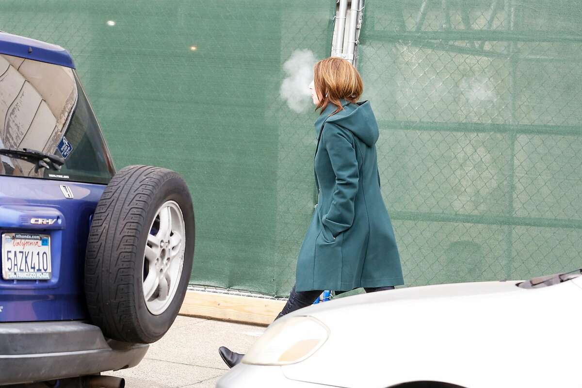 A woman exits Juul headquarters and begins to smoke a vape pen on Thursday, December 20, 2018 in San Francisco, Calif.