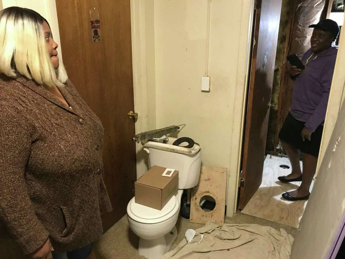 Keisha Taylor, left, looks at her apartment bathroom, which she can’t use for a week due to renovations by Charter Oak Communities, the city's housing authority.