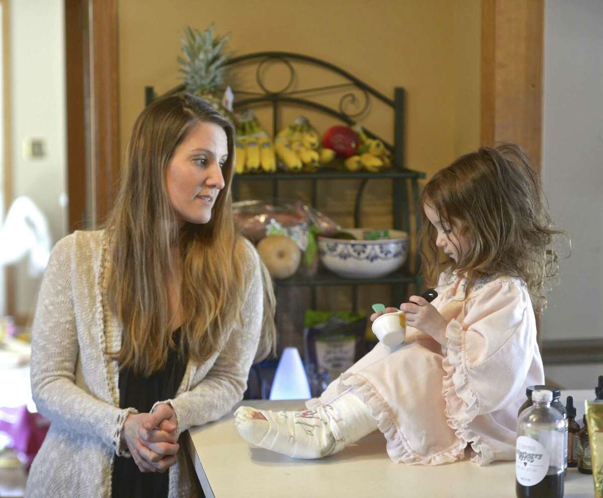 Katharine Pileggi watches as her daughter Emma, 3, takes a holistic treatment for inflammation on March 14 in Sherman.