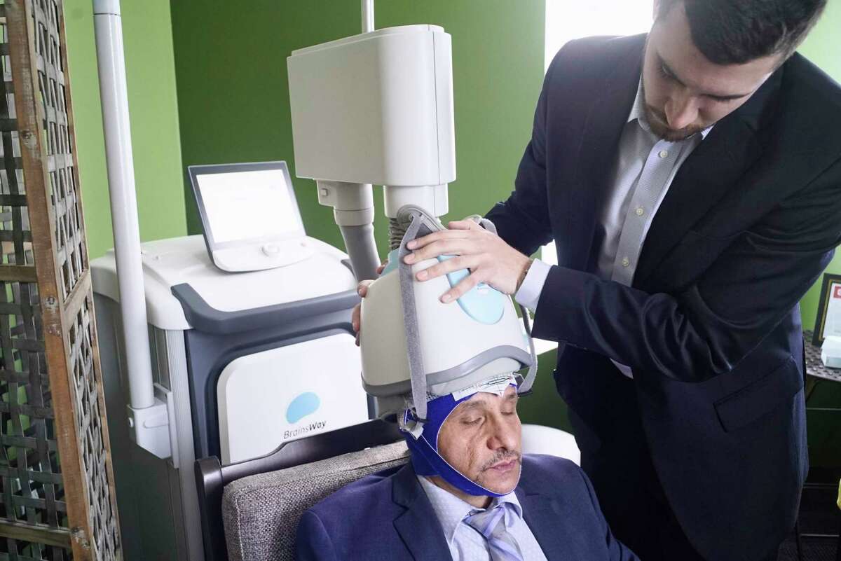Rocco Pezzulo, left, director of operations, sits for a demonstration on how the helmet is placed on the patient's head by John Seymour, a TMS specialist, for a Transcranial Magnetic Stimulation therapy session at Pinnacle Behavioral Health on Tuesday, March 19, 2019, in Albany, N.Y. Pezzulo said that he is also getting daily TMS therapy to help him think clearer, to be more focused and for what he calls peak performance. (Paul Buckowski/Times Union)