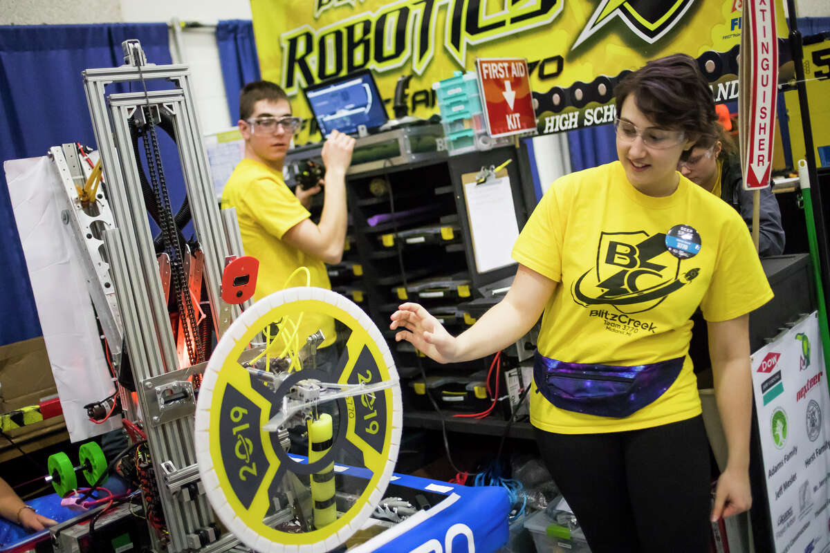 Members of Bullock Creek High School's robotics team demonstrate how their robot works for a young fan during the FIRST Robotics district competition on Saturday, March 23, 2019 at H. H. Dow High School. (Katy Kildee/kkildee@mdn.net)