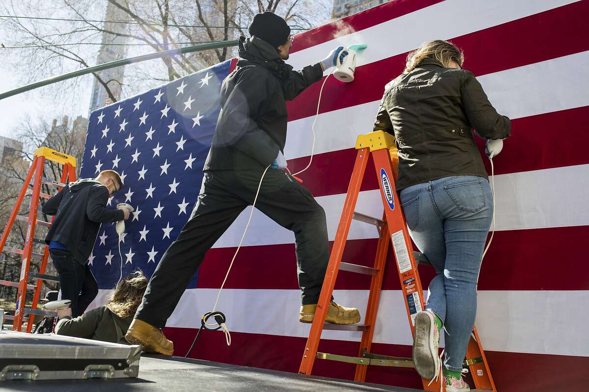 People steam an American flag that will serve as the backdrop for Sen. Kirsten Gillibrand, D-N.Y., before she kicks of her presidential campaign, Sunday, March 24, 2019, near the Trump International Hotel and Tower in New York. (AP Photo/Julius Constantine Motal)