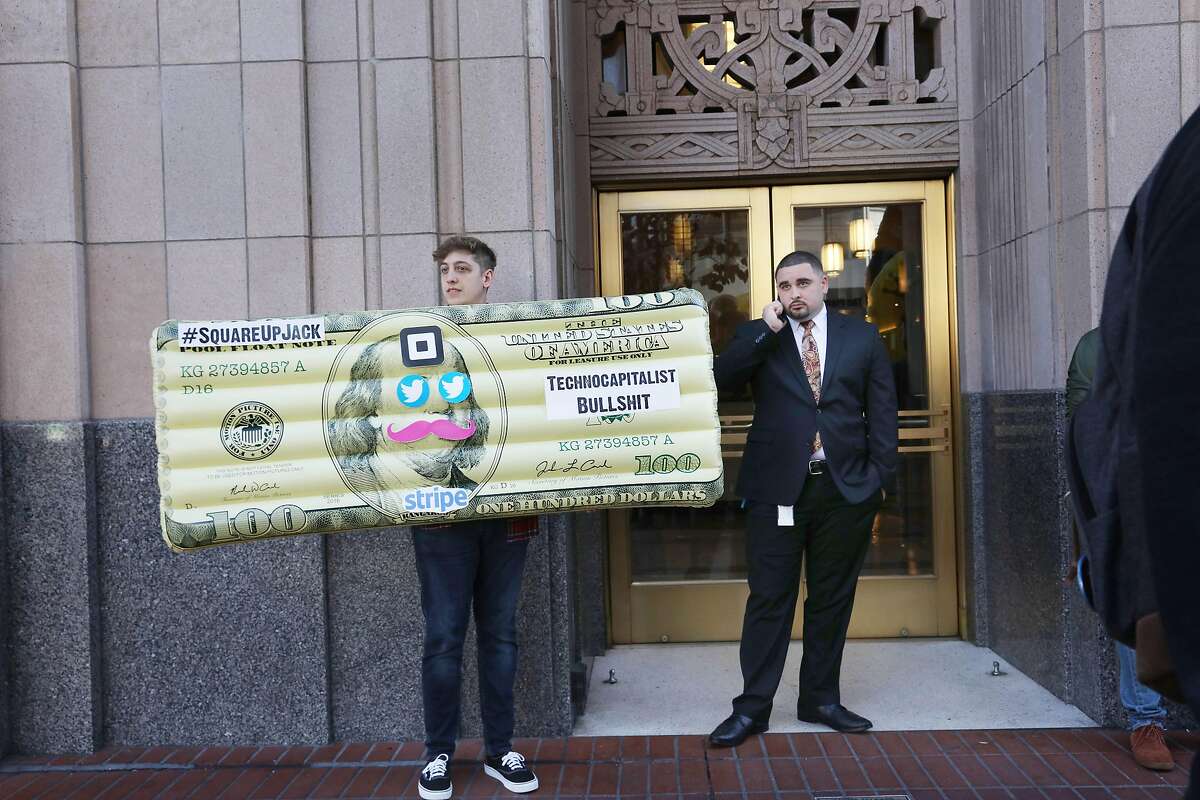 A tech worker who holds an inflated dollar bill with signs stuck on it stands in front of Twitter headquarters while attending aYes on C rally on Thursday, October 25, 2018 in San Francisco, Calif.