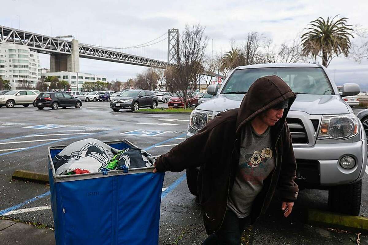 A homeless woman named Keri walks her belongings out of a parking lot that is situated next to the Watermark apartment complex in San Francisco, California, on Wednesday, March 27, 2019. The parking lot has been proposed by Mayor London Breed as a potential Navigation Center.