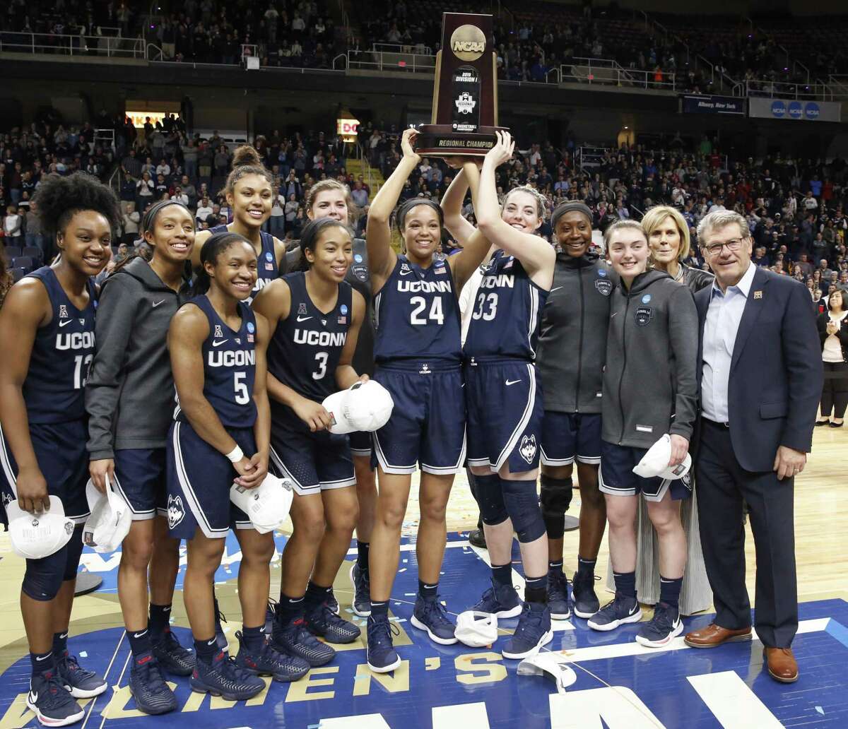 UConn players and coach Geno Auriemma, far right, celebrate with their trophy after winning the regional championship game in the NCAA women’s basketball tournament on Sunday.