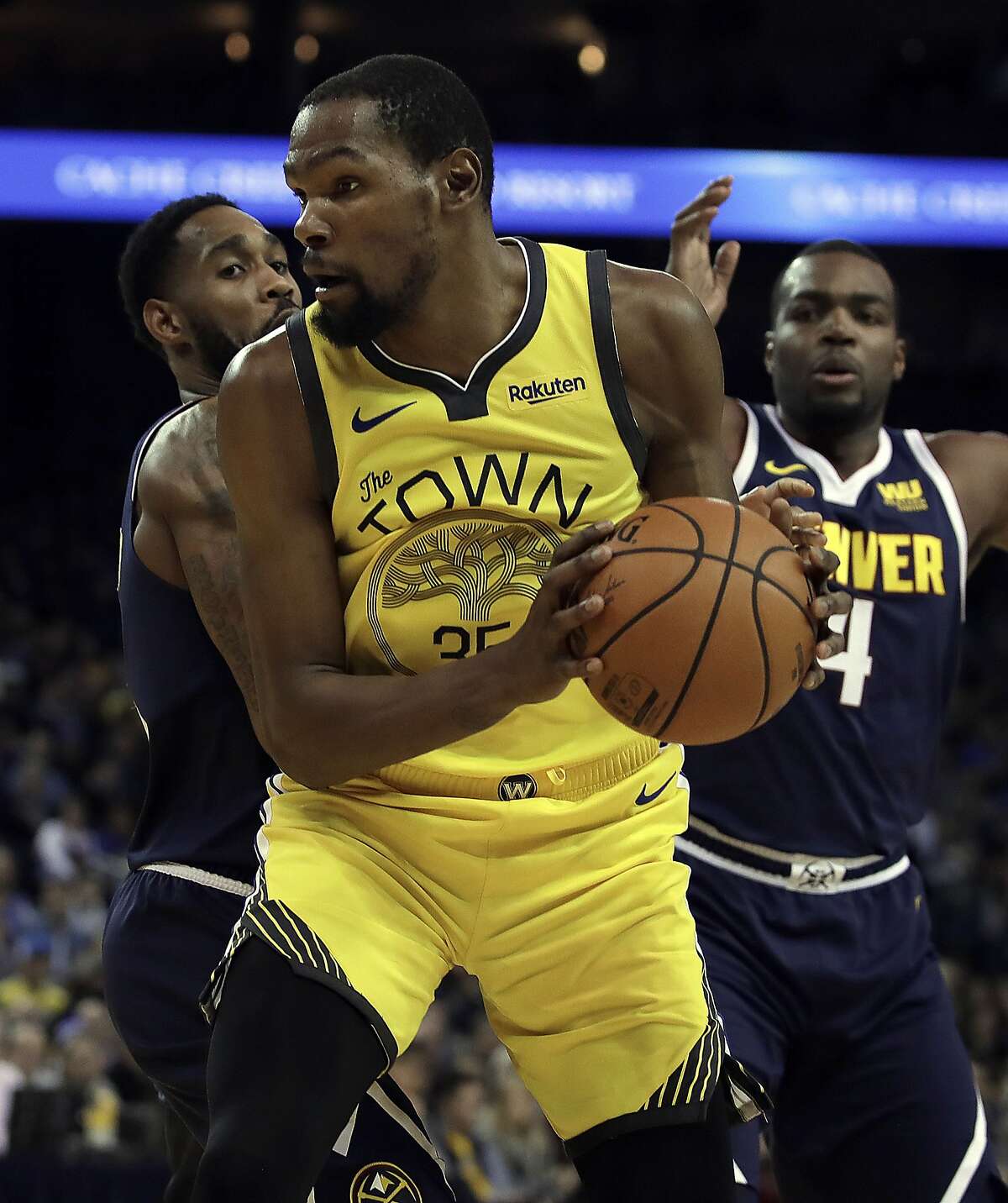 Golden State Warriors' Kevin Durant, center, looks to pass the ball away from Denver Nuggets' Will Barton, left, and Paul Millsap (4) during the second half of an NBA basketball game Friday, March 8, 2019, in Oakland, Calif. (AP Photo/Ben Margot)