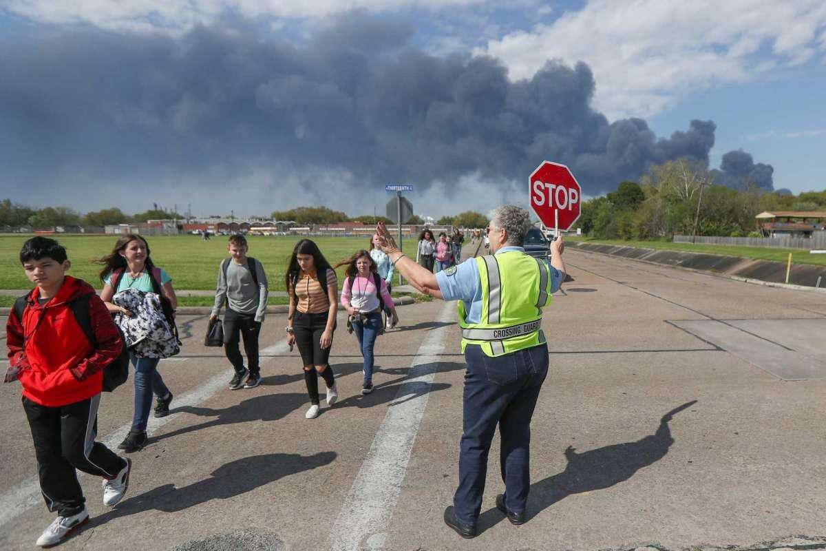 Deer Park Police Department crossing guard Adell Boren helps Deer Park Junior High School students at a crossing as the chemical fire burns in the background on March 19.