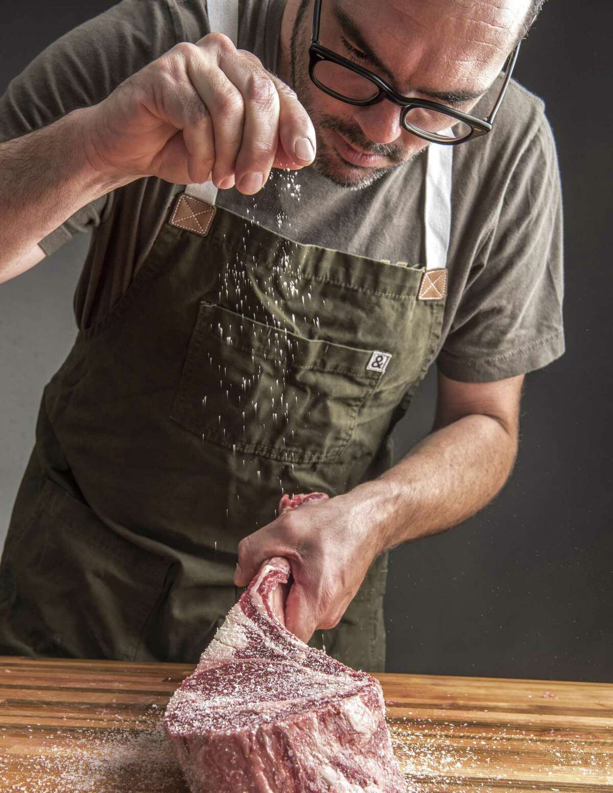 Aaron Franklin salting a bone-in ribeye steak from "Franklin Steak" by Aaron Franklin and Jordan Mackay.