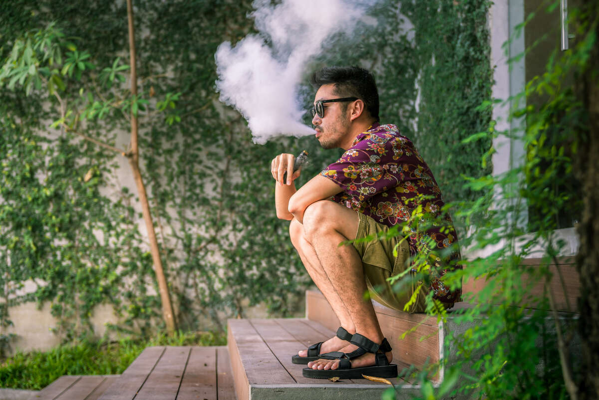 Man Using An Electric Cigarette A image of a young adult male has a cloud of nicotine vapor 'smoke' pouring from his mouth. Vape smoking, or 'vaping' is growing in popularity, as well as falling under stricter state and governmental regulations.